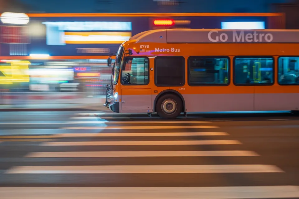 Orange Los Angeles Metro bus passing on blurred street at night.